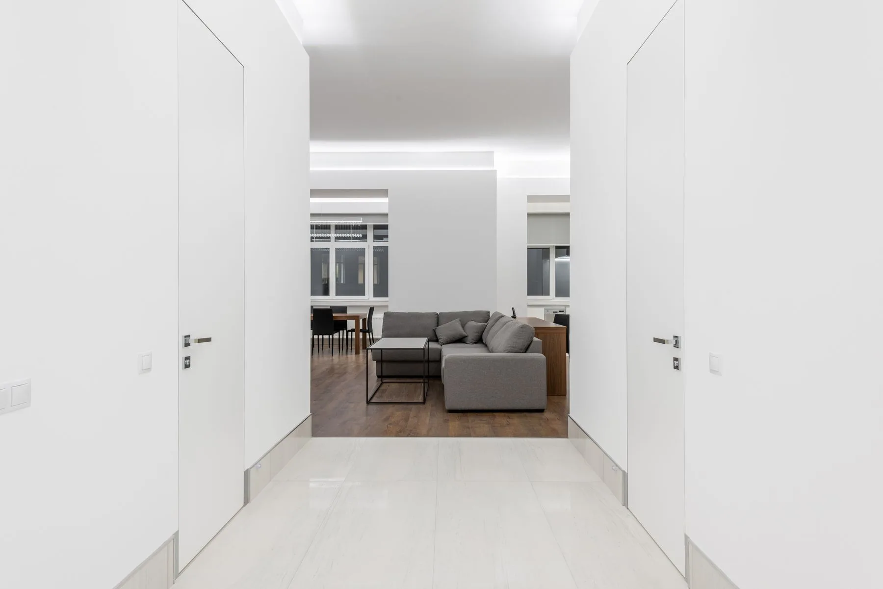 A bright living room with a gray sofa, wood flooring and simple white walls